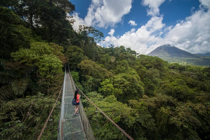 Puente colgante sobre el bosque tropical con el Volcán Arenal al fondo